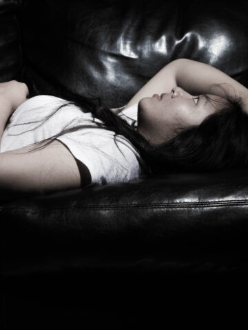Woman lying back on sofa looking overwhelmed