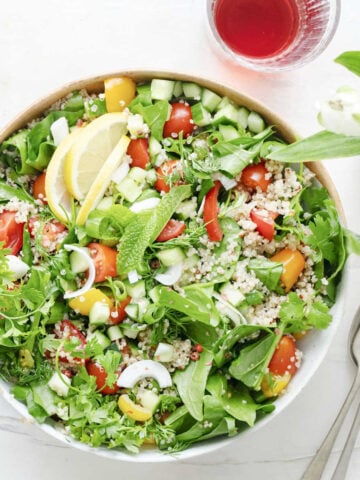 A big white bowl of salad and herbs with cutlery