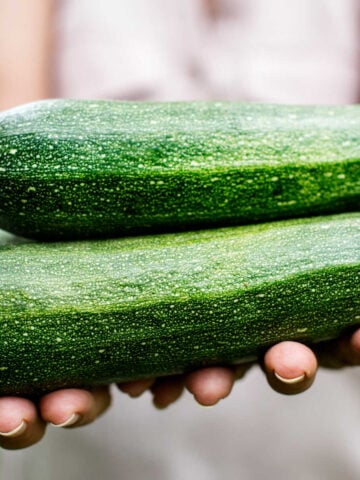 Two zucchini being held by a woman.