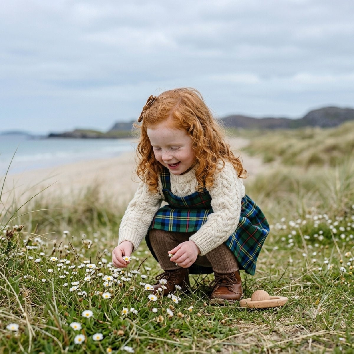Little Scottish girl with ginger hair picking daisies by the beach in Scotland